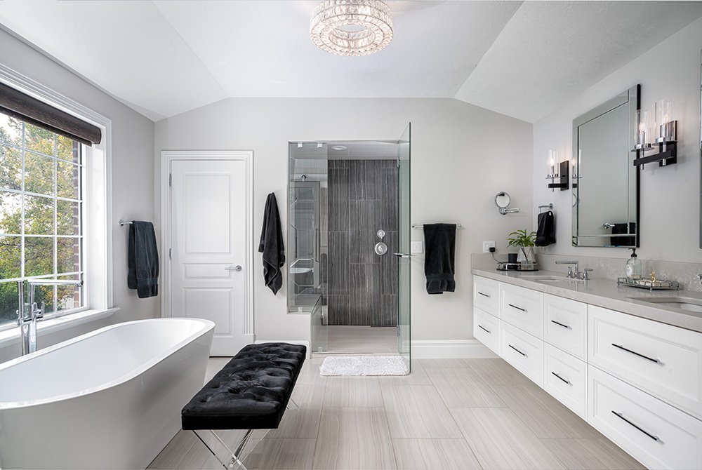 Modern bathroom featuring a freestanding bathtub, black cushioned bench, glass-enclosed shower, double sink vanity, white cabinetry, and large window with black blinds—crafted with quality by Residential Construction Services Utah.